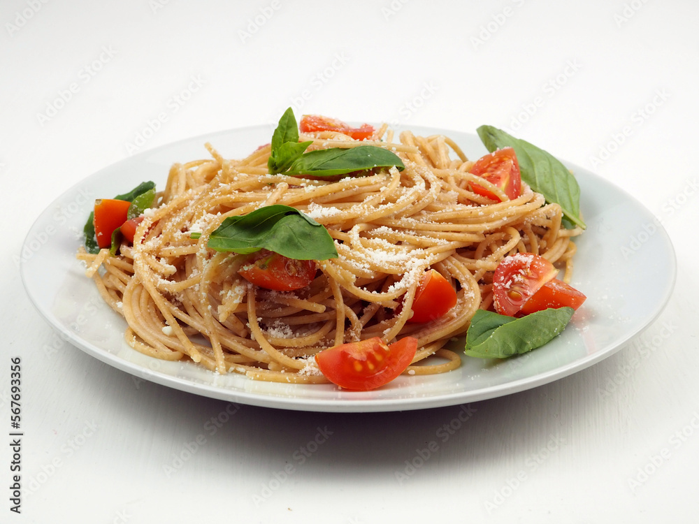 Close up of whole grain spaghetti pasta with cherry tomatoes, basil and parmesan cheese. Close up of whole grain spaghetti pasta with cherry tomatoes, basil and parmesan cheese.