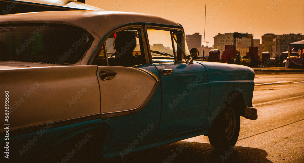 legant classic Cuban car cruises the Malecon with a stylish passenger, as the sun sets on Havana, Cuba