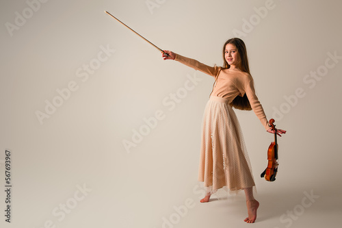 A girl in a long beige skirt plays the violin on a beige background.