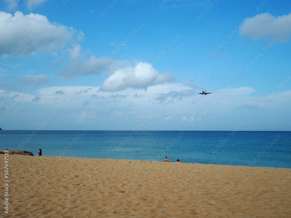 Beautiful atmosphere Overlooking the blue sky, calm sea, sandy beach, tourists are having fun playing in the water. And the plane is landing. View of Mai Khao Beach, Phuket, Thailand.
