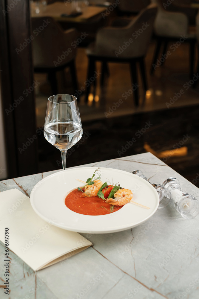 Gazpacho with shrimps. Serving food in a restaurant with glass of water and menu. Gazpacho with shrimps. Serving food in a restaurant with glass of water and menu.