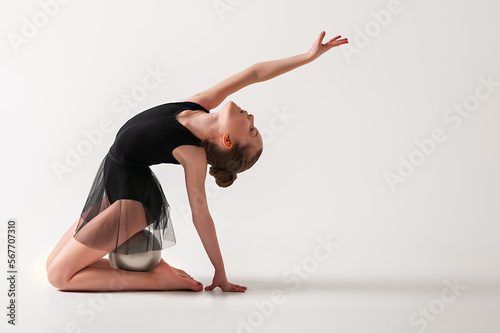 A girl in a gymnastic black bodysuit performs exercises with a ball. White background