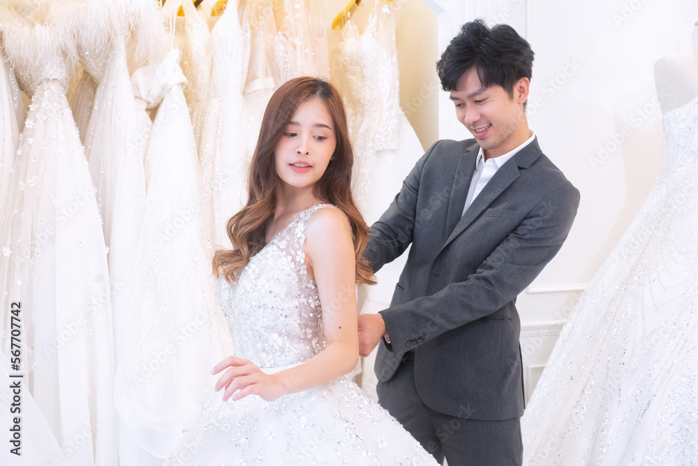 Beautiful young brunette love couple choosing wedding dress in a bridal salon man help zip up cloth