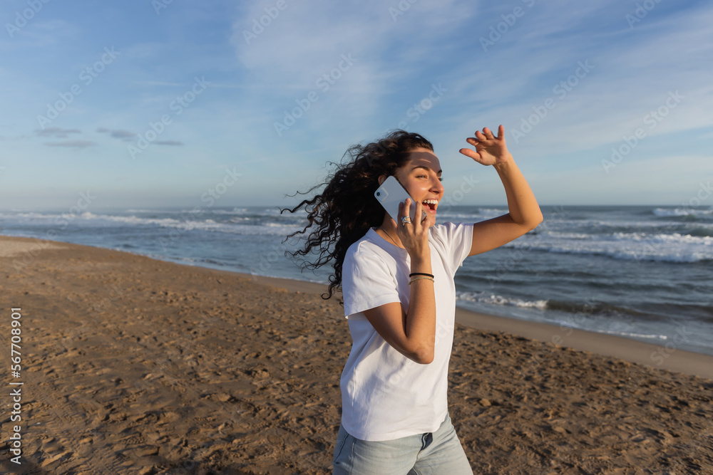 amazed woman in white t-shirt talking on smartphone on sandy beach in Barcelona. amazed woman in white t-shirt talking on smartphone on sandy beach in Barcelona.