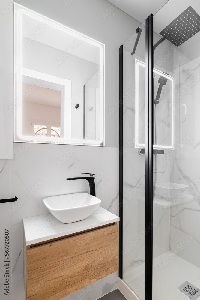 Obraz premium Bathroom with modern designer renovation and fittings. Vanity sink with black faucet. Walls of white granite with gray stains are beautifully illuminated by bright white light from square mirror.