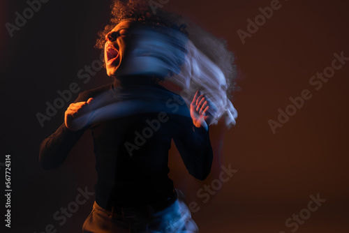 long exposure of injured and stressed african american man shouting on black background with orange and blue light