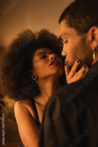 passionate african american woman touching face of young man while seducing him at home