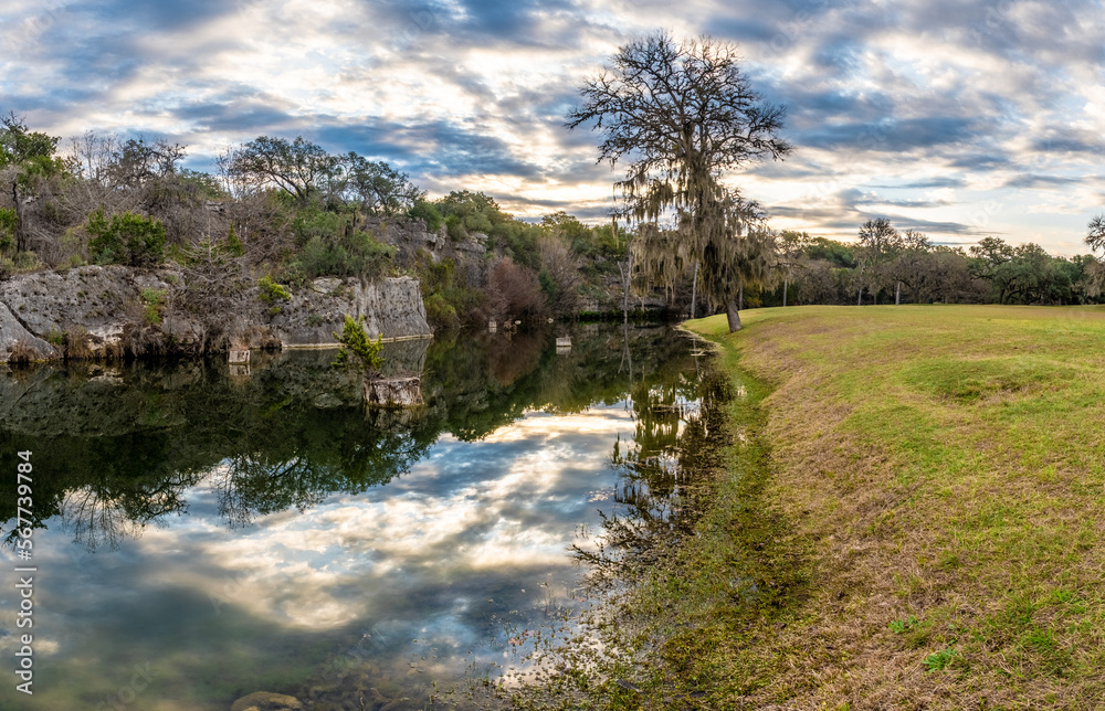 A creek flowing slowly along a rocky cliff with a loan tree on a grassy shore in winter, Swede Creek Park, Hill Country, Texas A creek flowing slowly along a rocky cliff with a loan tree on a grassy shore in winter, Swede Creek Park, Hill Country, Texas