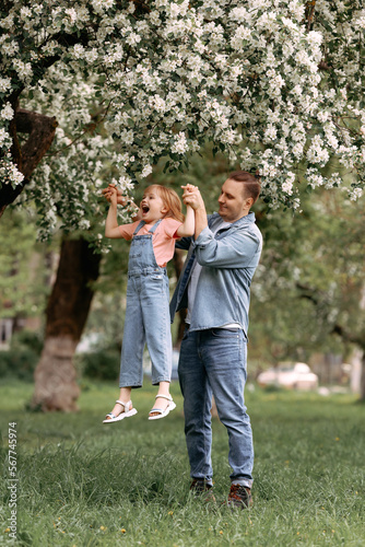 Dad and daughter are hugging under an apple blossom tree. A little girl in jeans hugs her dad. Spend time with your family in the park. Father's Day.