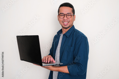 Adult Asian man smiling confident while working using his laptop photo