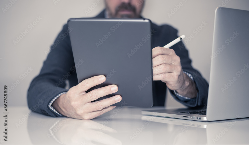 Businessman working with laptop and tablet sitting at the desk. Man write with electronic stylus pen Businessman working with laptop and tablet sitting at the desk. Man write with electronic stylus pen