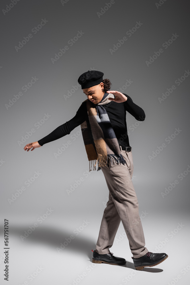 full length of young and stylish african american man in plaid scarf and beret stepping on grey background full length of young and stylish african american man in plaid scarf and beret stepping on grey background