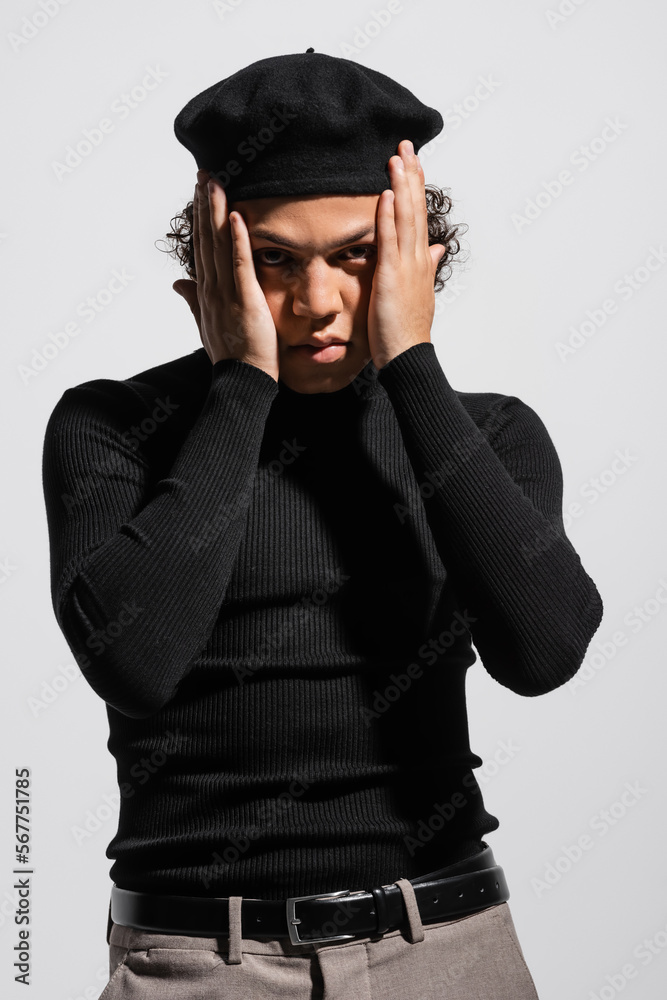 stylish african american man in black turtleneck and beret holding hands near face and looking at camera isolated on grey stylish african american man in black turtleneck and beret holding hands near face and looking at camera isolated on grey