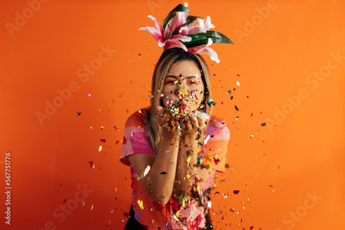 Brazilian Carnival. Studio shot of young woman celebrating carnival blowing confetti. Selective focus.