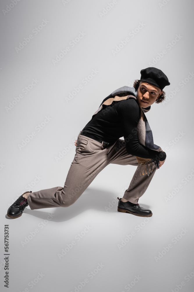full length of african american man in black pullover with plaid scarf and beret posing and looking away on grey background full length of african american man in black pullover with plaid scarf and beret posing and looking away on grey background