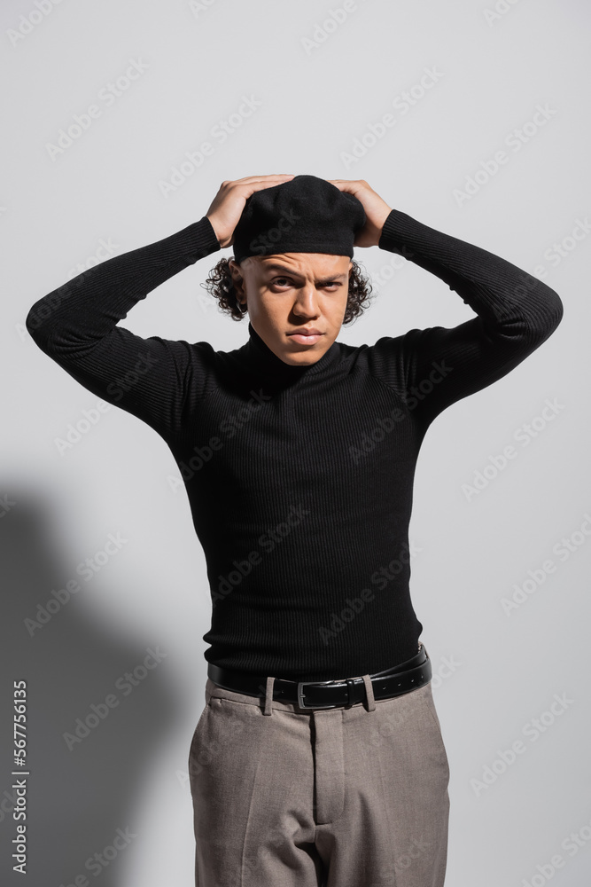 Obraz premium frowning african american man in black beret and turtleneck with trousers standing with hands on head on grey background