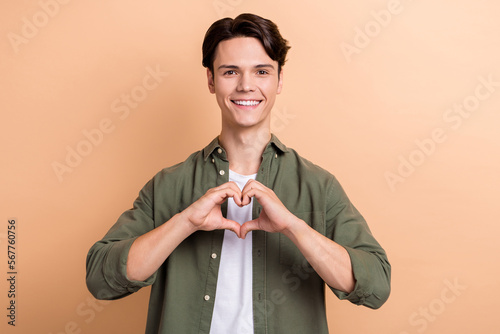 Photo of young positive student guy donator showing fingers love symbol charity for people with health problems isolated on beige color background photo