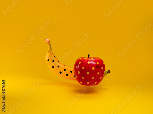 Close-up of an apple and banana painted with polka dots against a yellow background photo