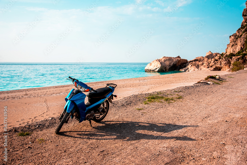 Summer landscape with a blue scooter by the sea on a background of rocks.