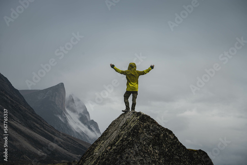 A man standing on a stone cliff in Akshayuk Pass, Nunnavut, Canada. Foggy mountains, cloudy morning in Buffin Island.