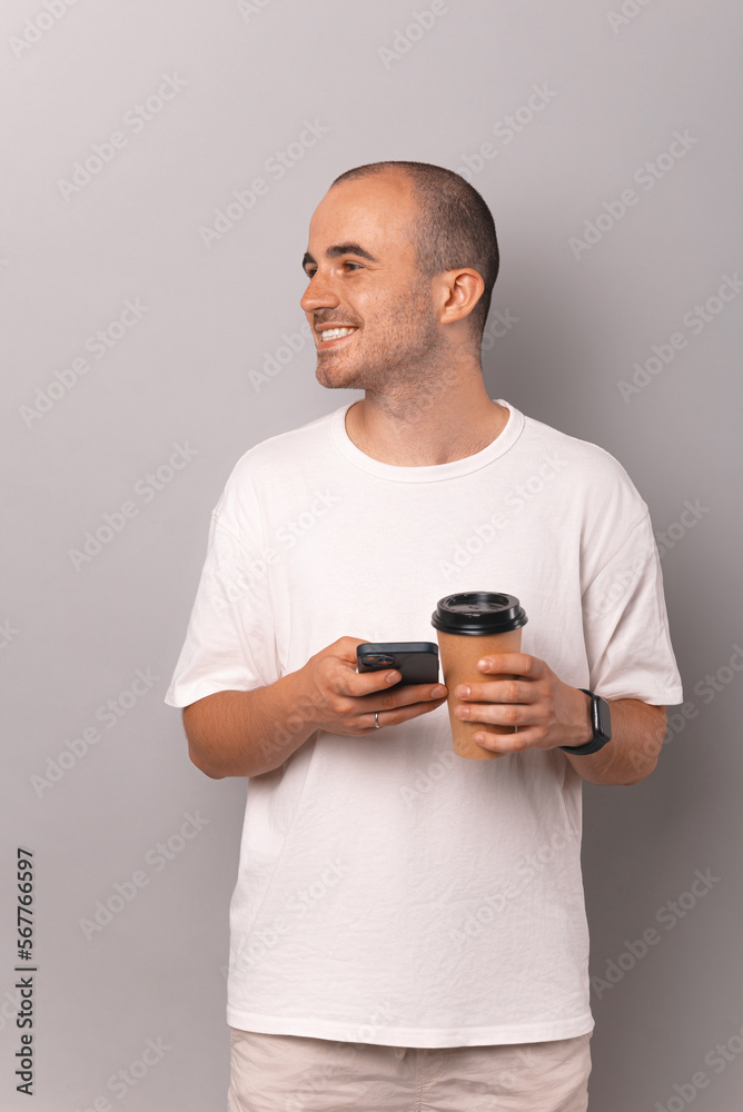 Vertical shot of a handsome young bald man holding phone and to go coffee cup. Vertical shot of a handsome young bald man holding phone and to go coffee cup.