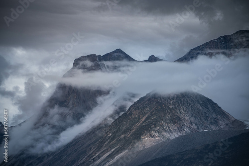 Scienic landscape with rocky mountain top in low clouds in gray cloudy sky. Akshayuk Pass, Baffin Island mountain seen through clouds. mountains background © Mariana Ianovska