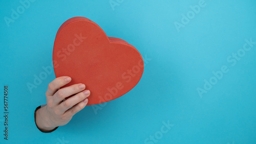 A woman's hand with a heart-shaped gift box sticks out of a blue paper background. 