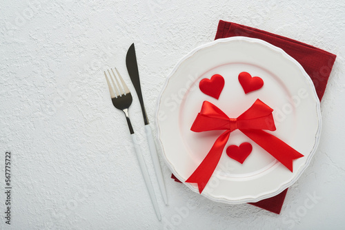 Valentines day romantic table setting. Empty or closeup of a dinner black plate, knife, fork and decorative silk hearts on white background. Holiday concept. Copy space for inscriptions.