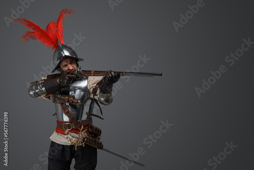 Studio shot of french rifleman dressed in plate armour aiming flintlock rifle.