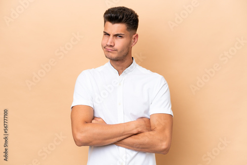 Young caucasian man isolated on beige background with unhappy expression