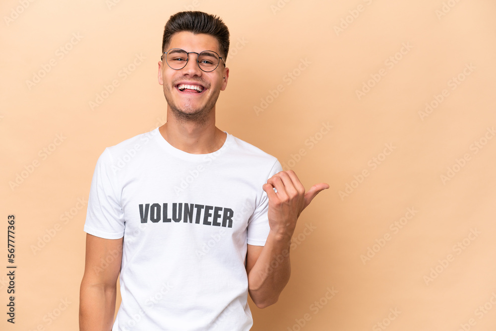 Young volunteer caucasian man isolated on beige background pointing to the side to present a product Young volunteer caucasian man isolated on beige background pointing to the side to present a product