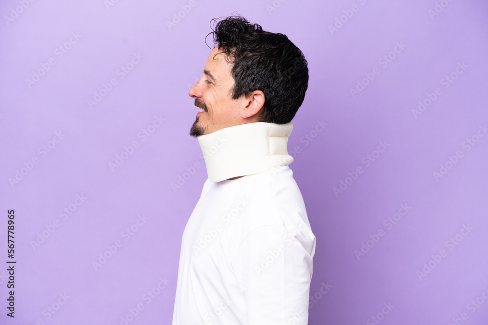 Obraz premium Young caucasian man wearing neck brace isolated on purple background looking side