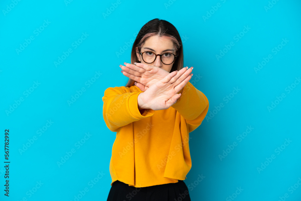 Young caucasian woman isolated on blue background making stop gesture with her hand to stop an act