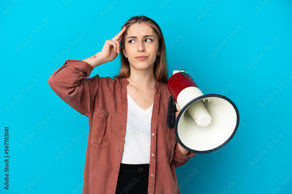 Young caucasian woman isolated on blue background holding a megaphone and having doubts Young caucasian woman isolated on blue background holding a megaphone and having doubts