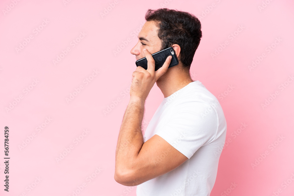 Young caucasian man isolated on pink background keeping a conversation with the mobile phone with someone Young caucasian man isolated on pink background keeping a conversation with the mobile phone with someone
