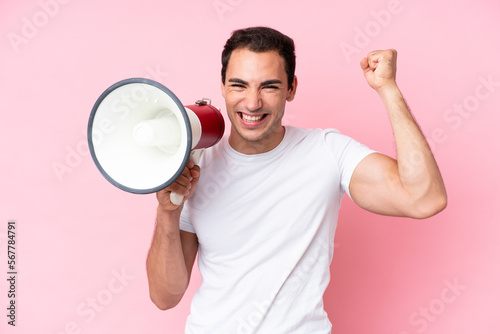 Young caucasian man isolated on pink background shouting through a megaphone to announce something
