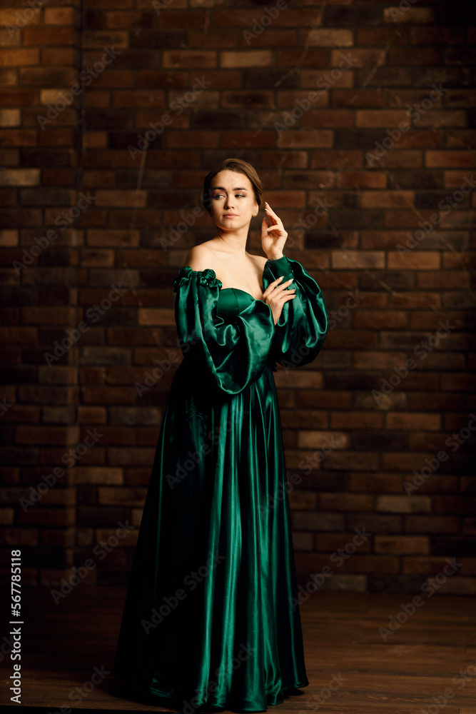Full-length portraits of a girl in a green dress against a brown brick wall Full-length portraits of a girl in a green dress against a brown brick wall
