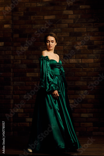 Full-length portraits of a girl in a green dress against a brown brick wall