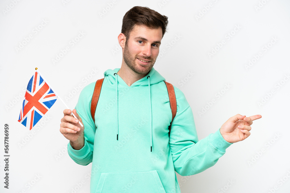 Young student caucasian man holding an United Kingdom flag isolated on white background pointing finger to the side
