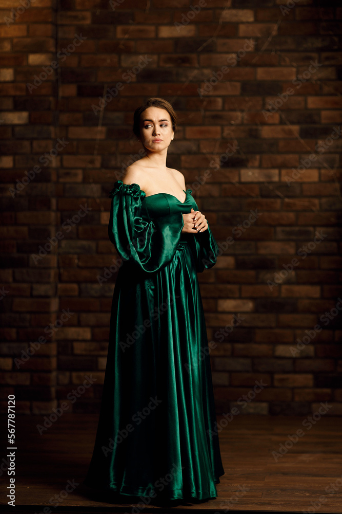 Full-length portraits of a girl in a green dress against a brown brick wall