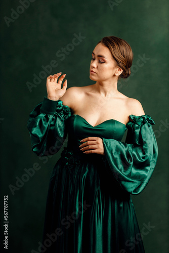 waist portrait of a girl in a green dress standing against a green wall © artem