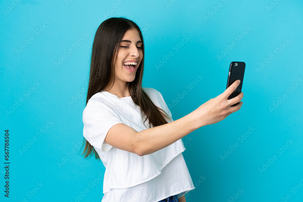 Young caucasian woman isolated on blue background making a selfie with mobile phone Young caucasian woman isolated on blue background making a selfie with mobile phone