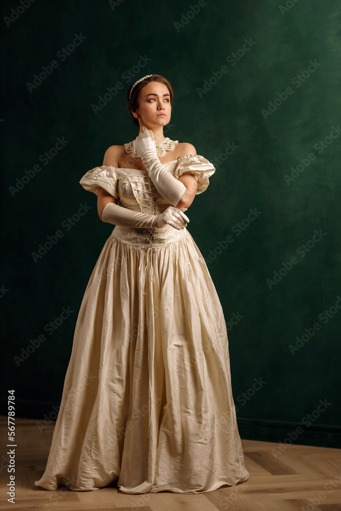 full-length portrait of a girl in a beige dress standing against a green wall full-length portrait of a girl in a beige dress standing against a green wall