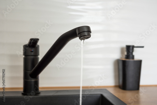 Black kitchen faucet with a little flowing water. Water shortage concept