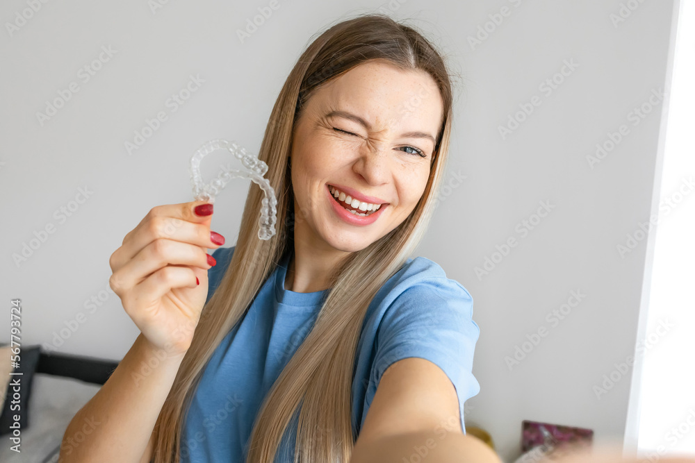 Cheerful girl make selfie holding an invisible braces aligner, recommending this new treatment. Dental healthcare concept. Cheerful girl make selfie holding an invisible braces aligner, recommending this new treatment. Dental healthcare concept.