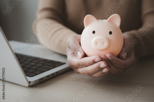 Woman working on laptop beside piggy bank for work and saving concept