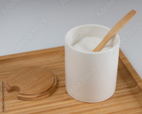 Kitchen jar with white sugar. Wooden spoon and stand. Sweet ingredient for dessert. Closeup photo