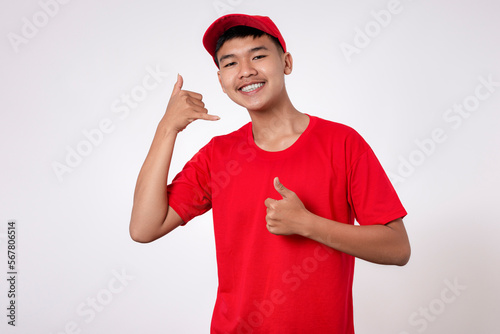 Phones calling concept. Smiling young asian Delivery man in red uniform isolated on white background making phone gesture, calling gesture