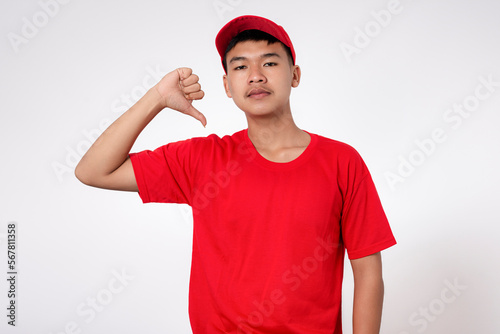 Courier Delivery worker shipping concept. Smiling young asian Delivery man in red uniform isolated on white background doing negative thumbs down gesture with hand and fingers.