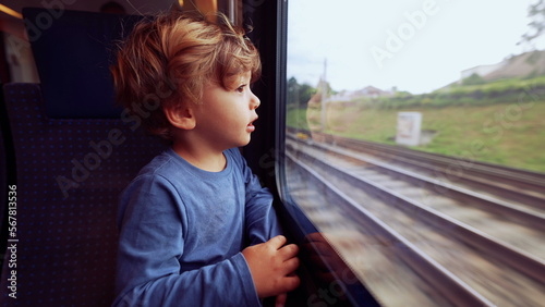 Child travels by train looking outside through window glass